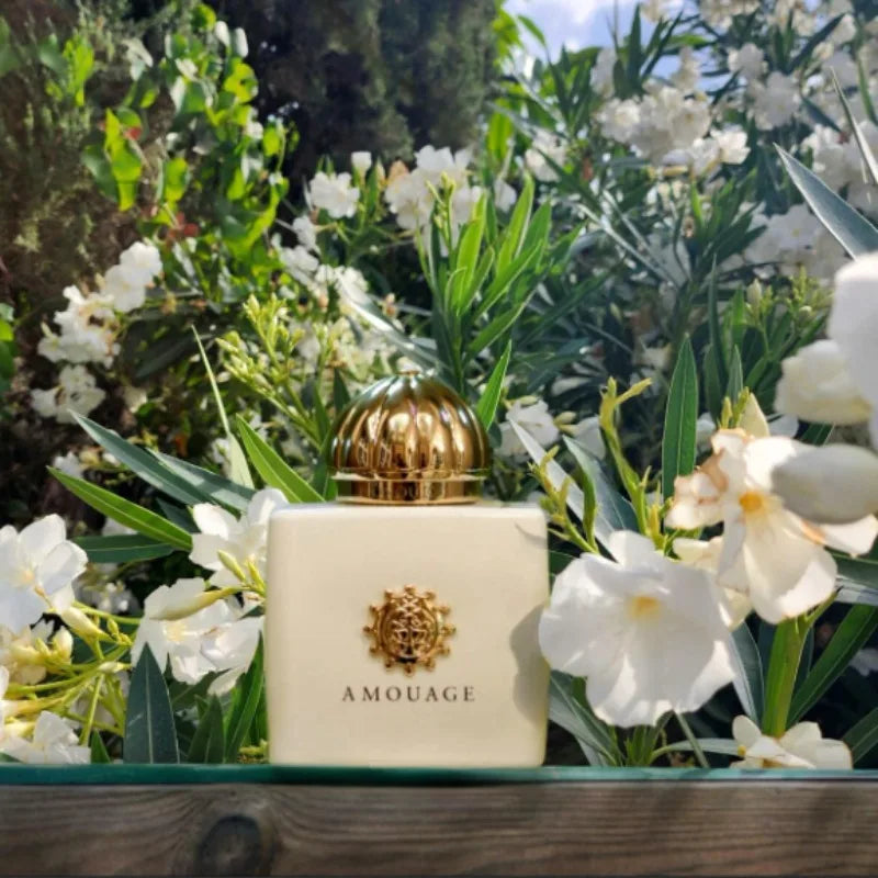 Amouage Guidance 46 perfume bottle: matte cream square glass, gold domed cap and crest, set against white flowers.