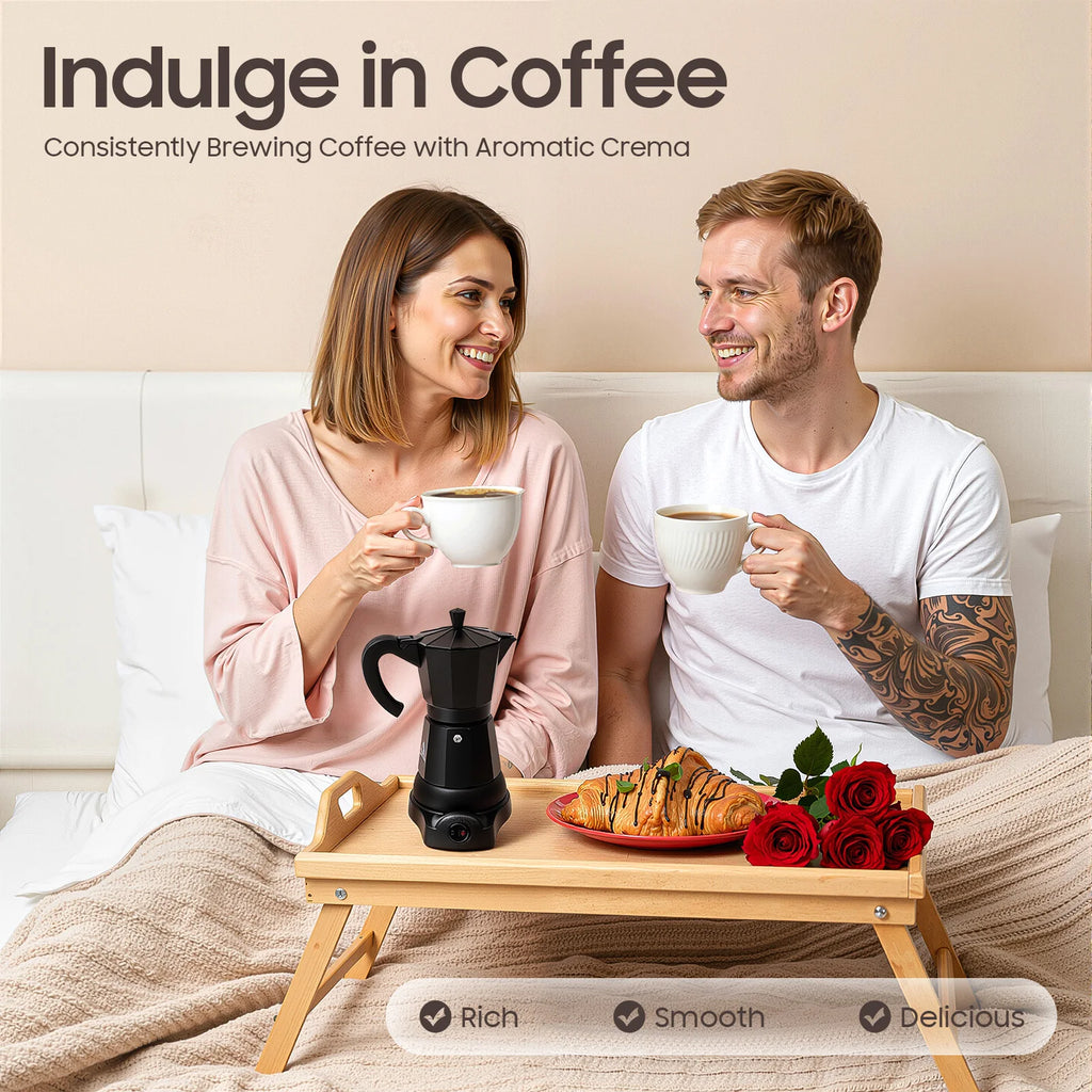 Couple in bed with a black electric moka pot coffee maker on a wooden breakfast tray with croissants and red roses.