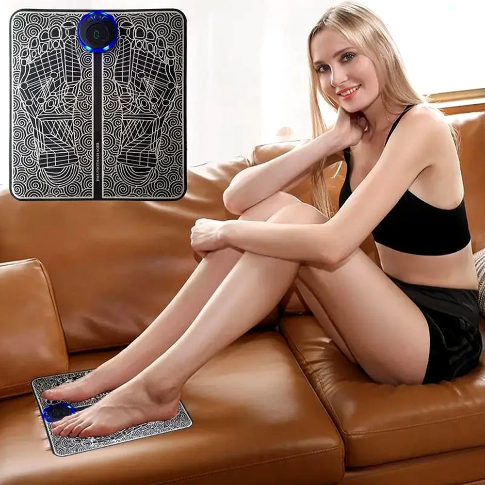 Woman using black EMS foot massage mat with blue LED controller for relaxation and sore feet relief on a sofa.