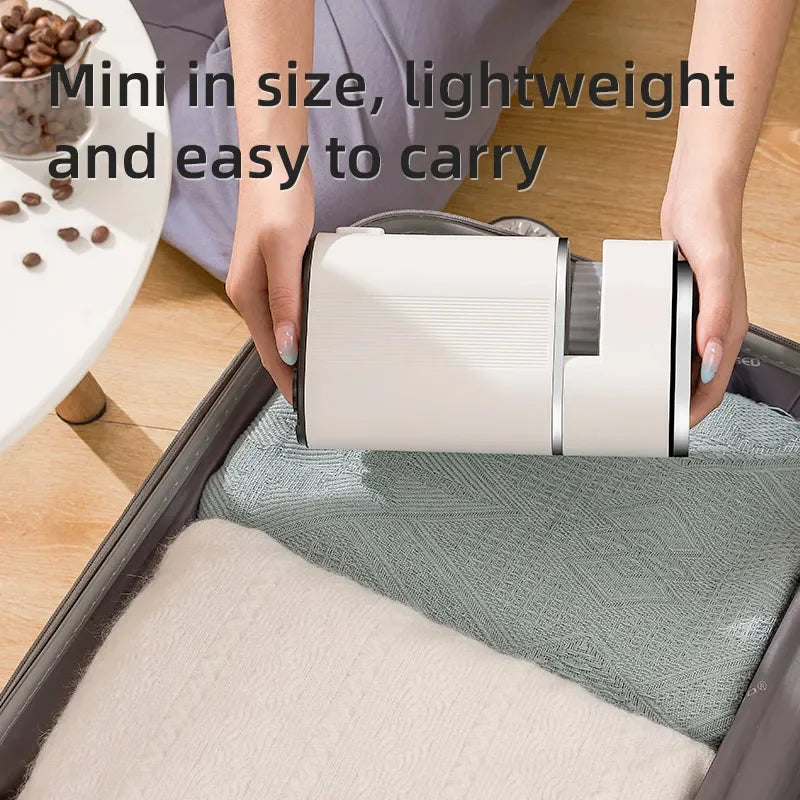 Portable white mini coffee grinder held over a suitcase, showcasing a compact and lightweight travel design.