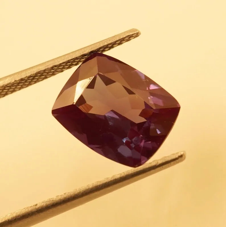 Faceted cushion-cut alexandrite gemstone, deep red with warm amber flashes color change