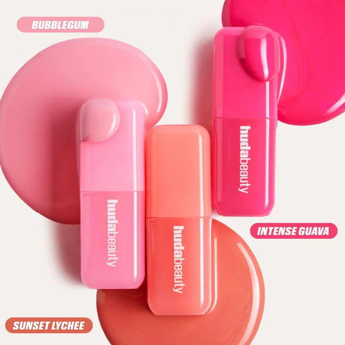 Huda Beauty hydrating lip and cheek blush sticks in Bubblegum, Sunset Lychee, and Intense Guava cream pigment textures.