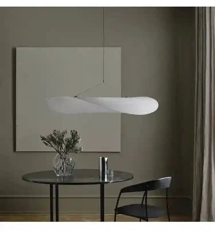 White fabric pendant light with an elongated, organic wave shape suspended over a dining table.