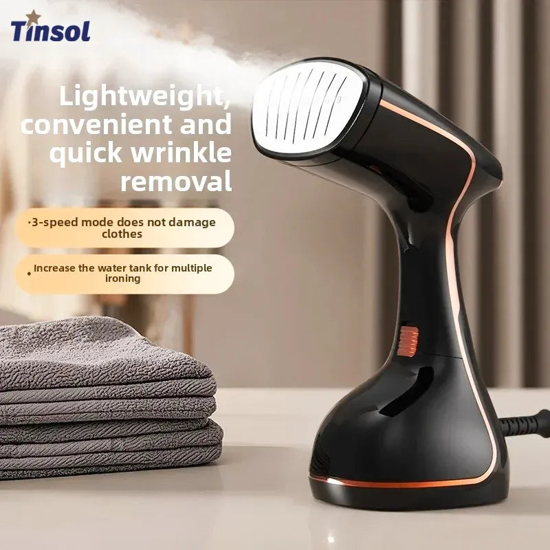 Tinsol handheld garment steamer in black and rose gold emitting steam beside folded clothes, for quick wrinkle removal.